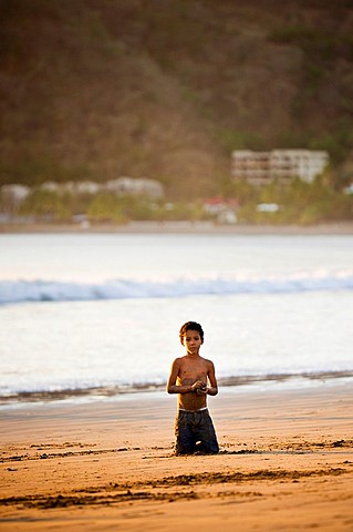 Little boy kneeling in the sand on the shore of San Juan del Sur, Nicaragua