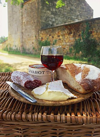 Still life of bread, glass of red wine, cheese and sausage, picnic meal on top of a wicker basket, in the Dordogne, France, Europe