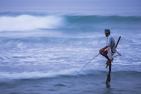 Stilt fishing, a stilt fisherman in the waves at Midigama near Weligama, South Coast, Sri Lanka, Asia