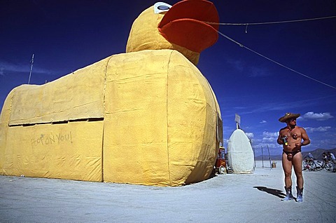 A man stands next to a giant duck at Burning Man in the Black Rock Desert, Nevada on August 29, 2002.  Burning Man is an art festival that celebrates free expression.  In 2002 about 29,000 people attended the festival that started in 1986 when Larry Harvey