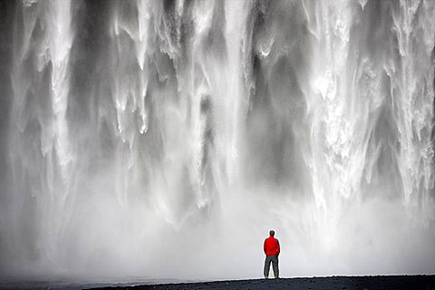 Man in red jacket standing in front of the 62m high Skogafoss waterfall near the village of Skogar, southern area, Iceland, Polar Regions