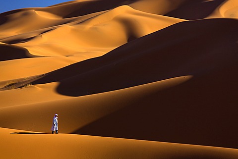 Berber man walking among the orange sand dunes of the Erg Chebbi sand sea, Sahara Desert near Merzouga, Morocco, North Africa, Africa